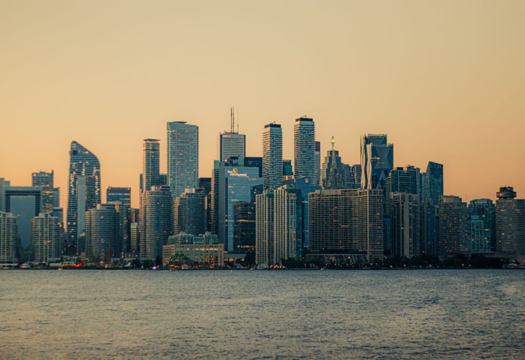 Toronto skyline with modern skyscrapers reflecting sunset light across Lake Ontario.